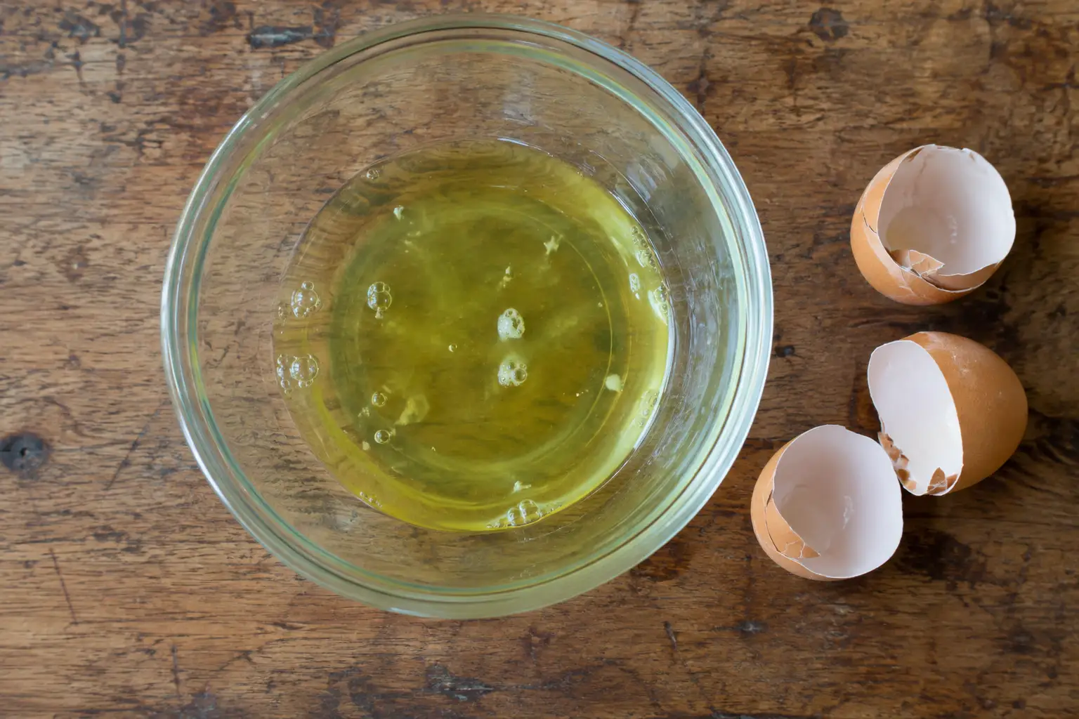 A raw egg white in a glass bowl beside cracked eggshells, nutrition facts and calories for one egg white