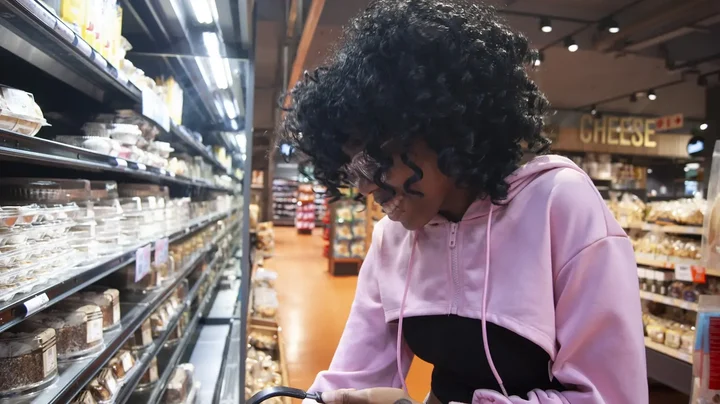 A young woman shopping in a grocery store aisle, checking products she logs most often