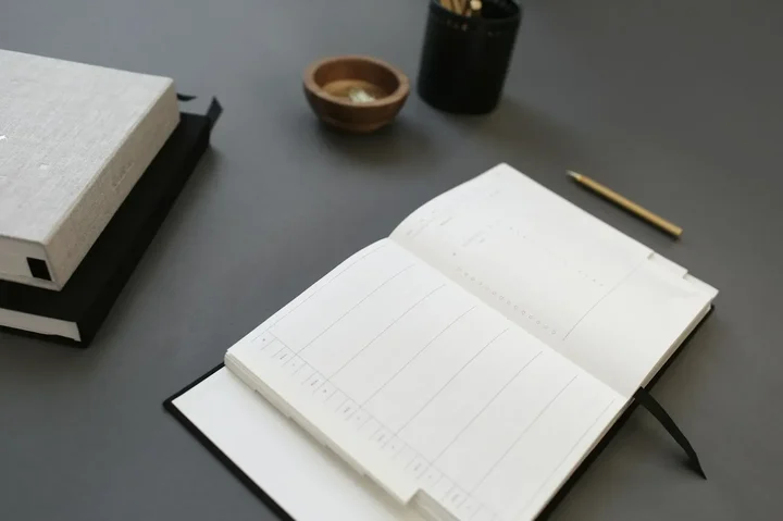 An open paper planner on a dark desk with a pen beside it