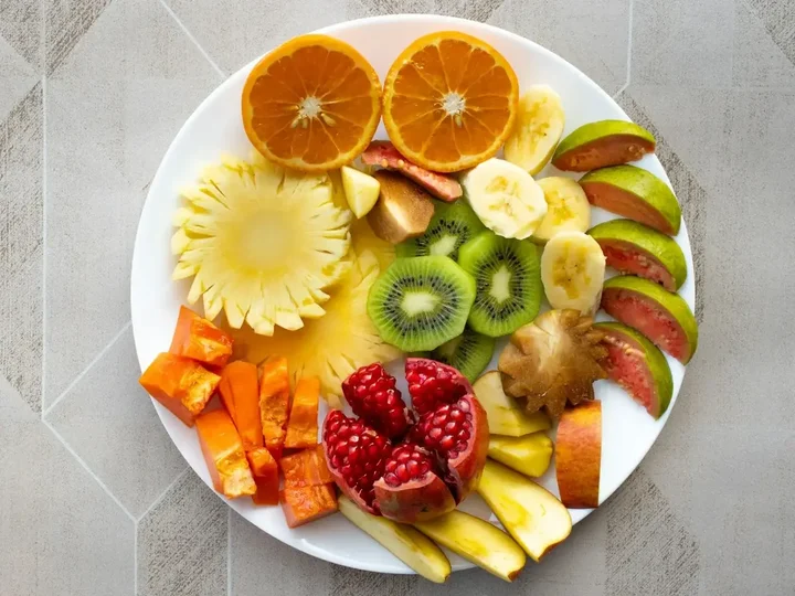A white plate of sliced oranges, kiwi, pineapple, papaya, pomegranate and guava