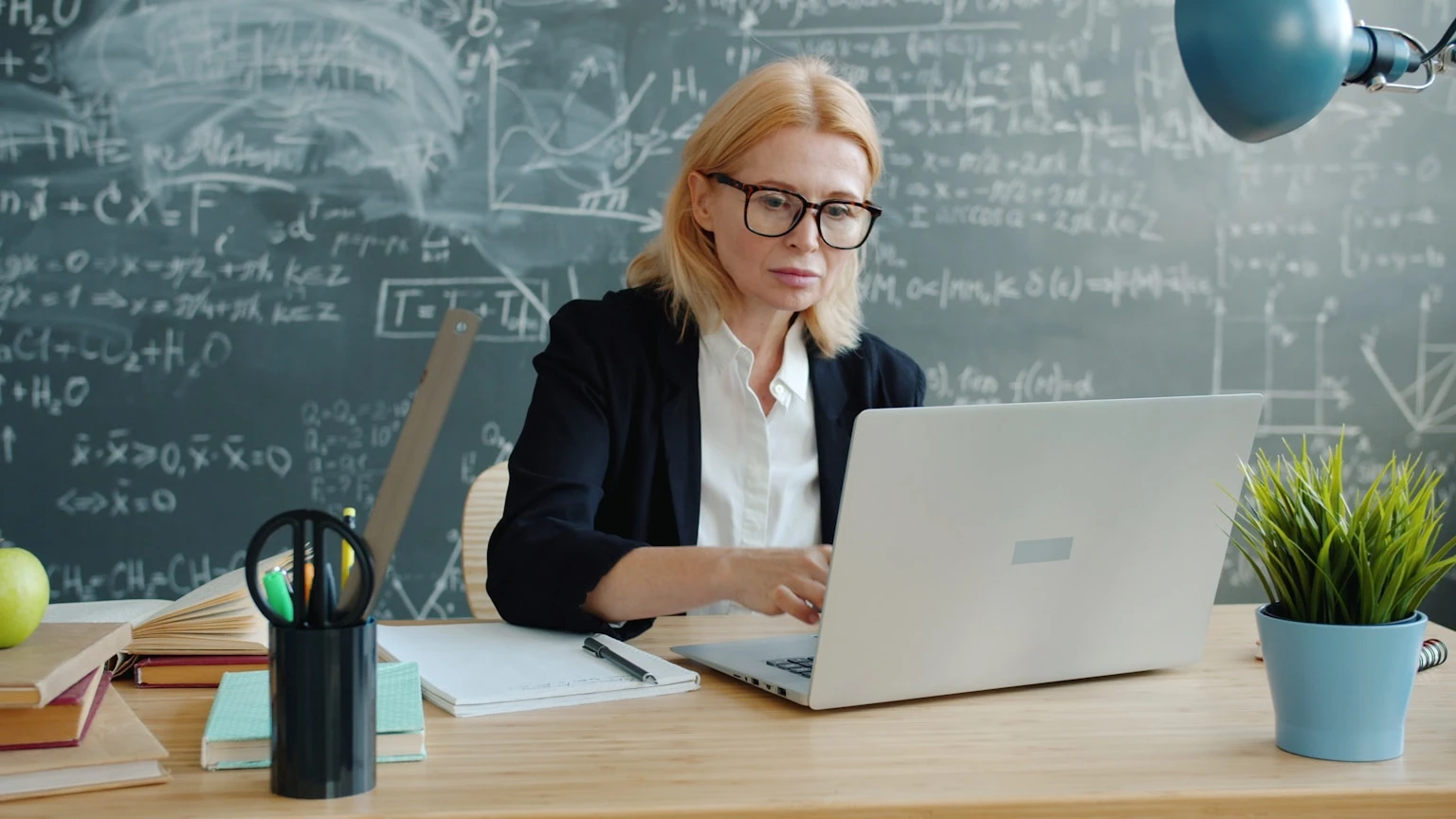 Student working on a laptop in front of a chalkboard, representing back-to-school deals